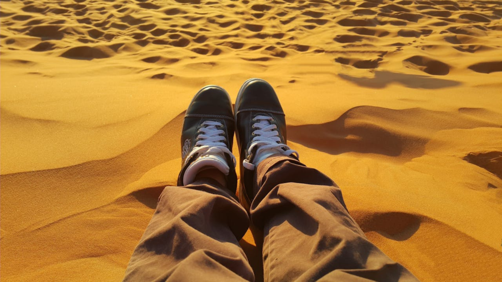 Person's feet in sneakers on golden desert sand dunes