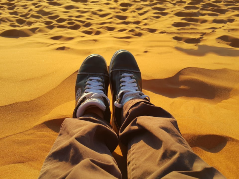 Person's feet in sneakers on golden desert sand dunes