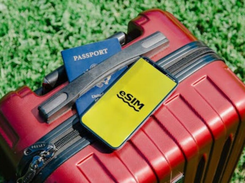 Red luggage with passport, eSIM card, and travel accessories on grass