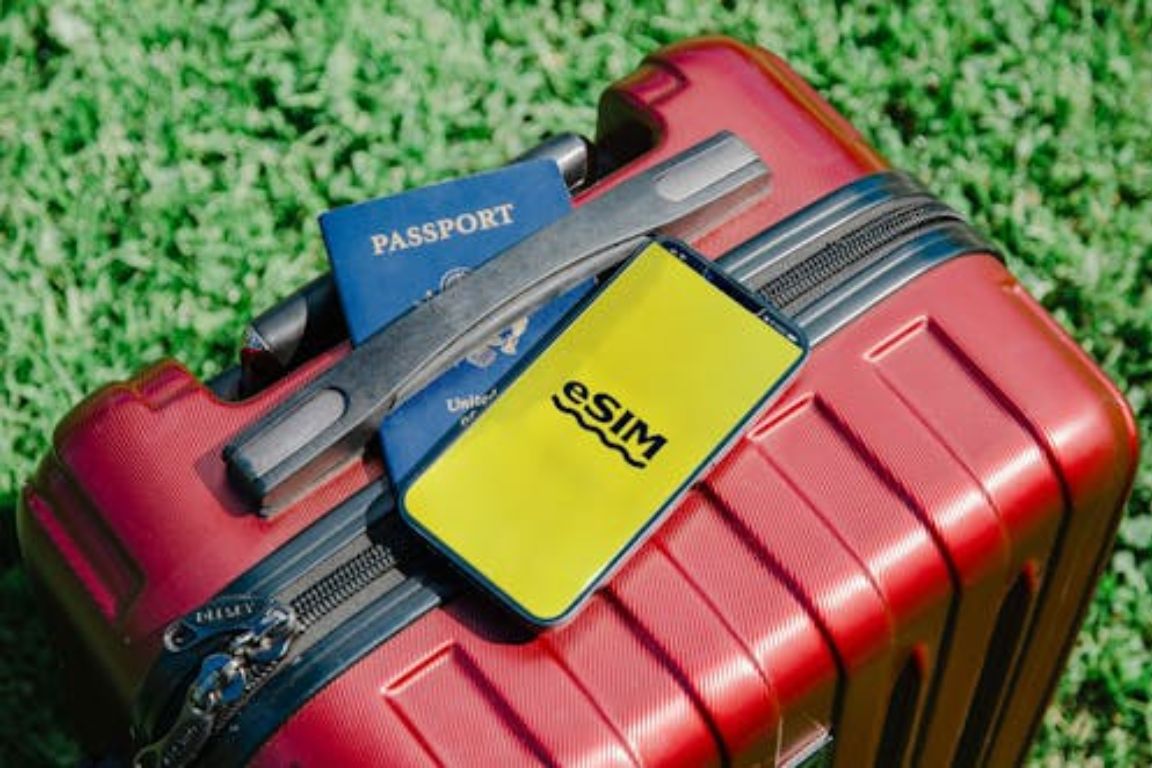Red luggage with passport, eSIM card, and travel accessories on grass