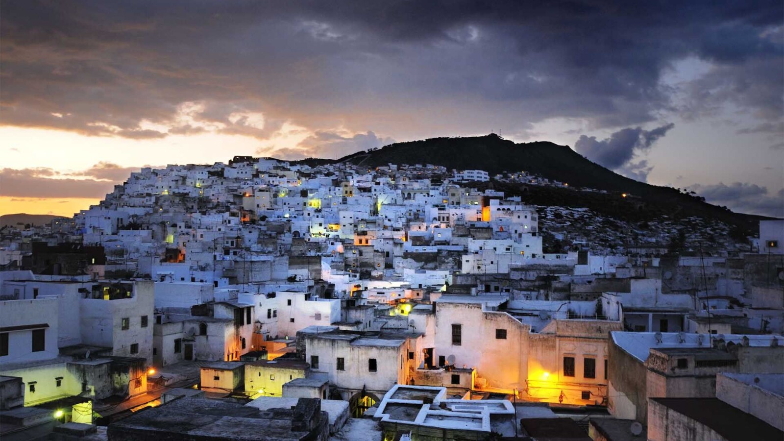 White-washed hillside town at dusk with glowing windows Morocco