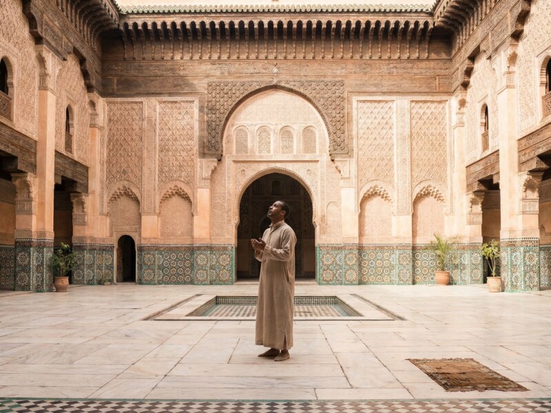 Nearly empty Ben Youssef Medersa courtyard in Marrakech during Ramadan with single visitor admiring intricate Islamic tilework and carved architecture