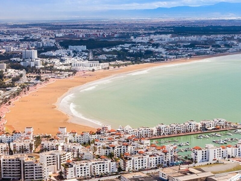 Aerial view of Agadir’s crescent-shaped sandy beach, turquoise Atlantic waters, and white resort buildings lining the marina and coastline in southern Morocco