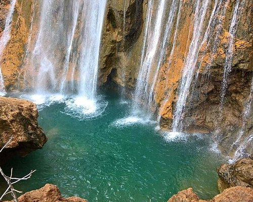 Cascading Imouzzer waterfalls plunging down rugged orange rock cliffs into a deep turquoise natural pool in the Atlas Mountains near Agadir, Morocco