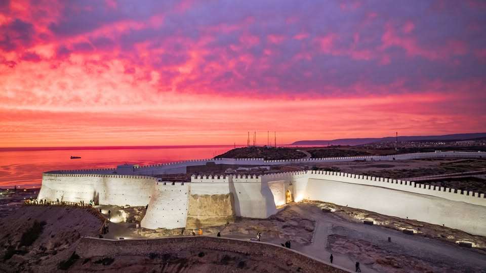 Illuminated walls of Kasbah Agadir Oufella overlooking the Atlantic at dusk, with a dramatic pink and purple sunset sky glowing above the historic hilltop fortress in Agadir, Morocco