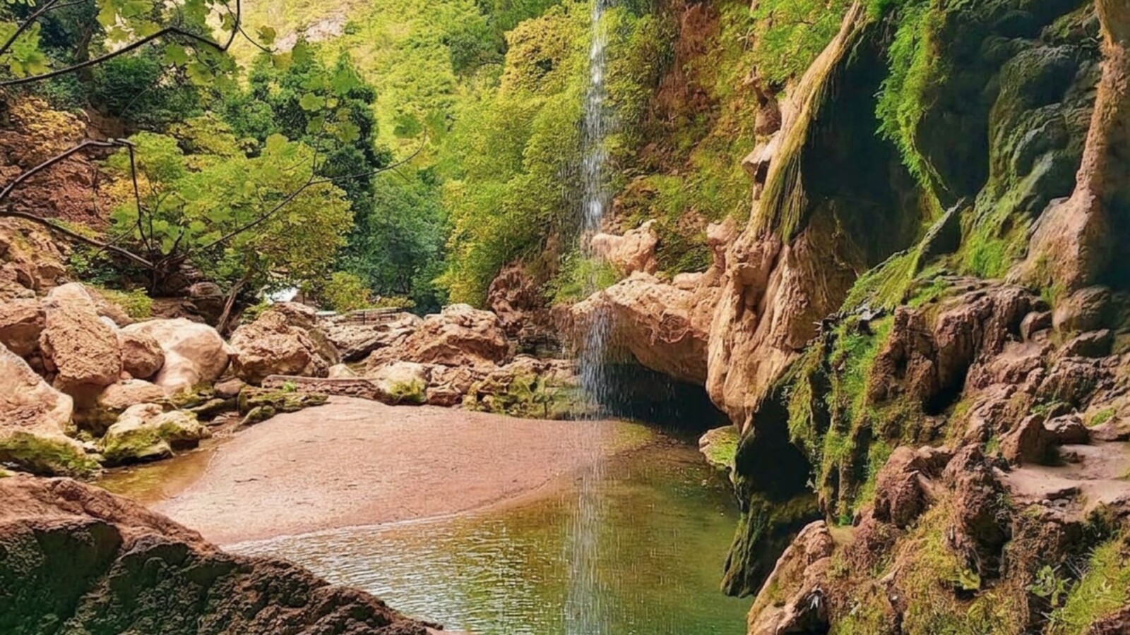 Akchour waterfall in Morocco, with a rocky pool, moss-covered cliff walls, and a narrow cascade falling into the water.