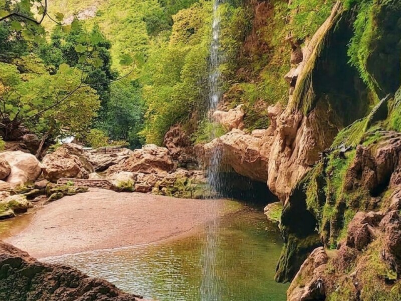 Akchour waterfall in Morocco, with a rocky pool, moss-covered cliff walls, and a narrow cascade falling into the water.