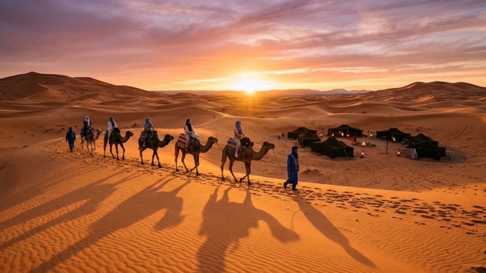 Camel caravan crossing the Erg Chebbi dunes at sunset toward a Berber desert camp on a Sahara tour from Marrakech.