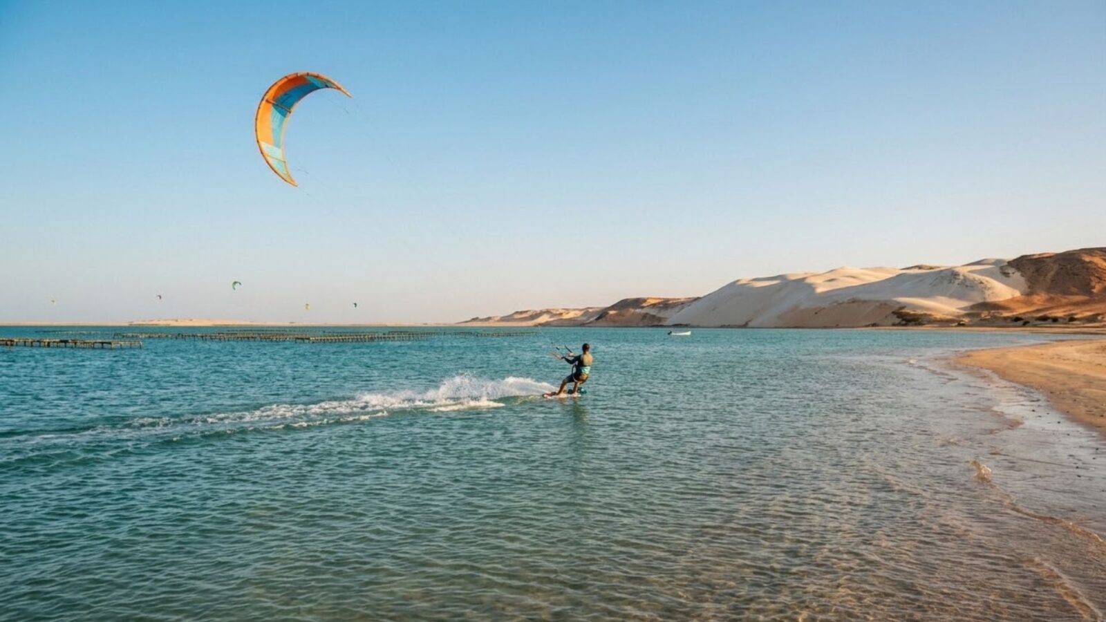 Kitesurfer riding flat turquoise water in the Dakhla lagoon with white Sahara dunes in the background at golden hour